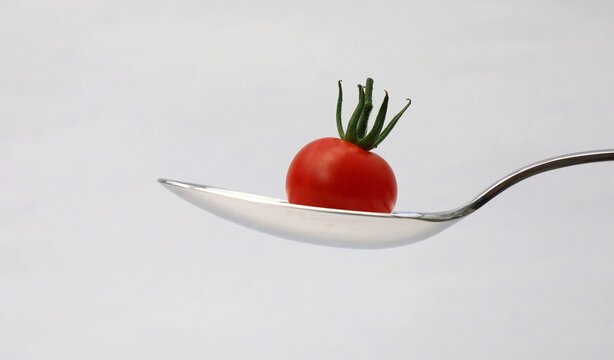 Tablespoon with pasta and cherry tomato, on white background.