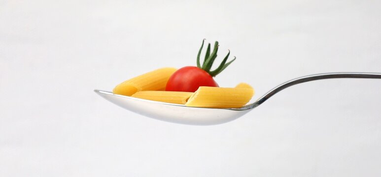 Tablespoon with pasta and cherry tomato, on white background.
