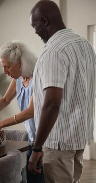Diverse senior couple arriving home carrying bag, unpacking olive oil, viewing recipe on smartphone
