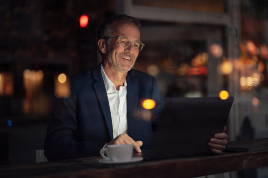 Happy businessman with eyeglasses working on laptop at night