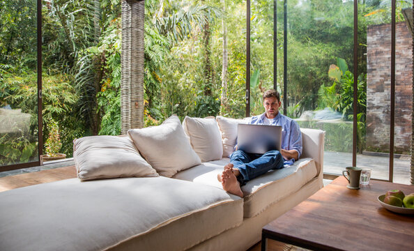 Freelancer sitting on sofa and using laptop at home