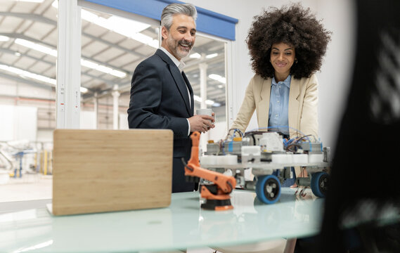 Smiling businessman with businesswoman looking at model of robotic vehicle in factory