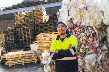 Portrait of a smiling latin worker posing with crossed arms in a recycling center, with a large...