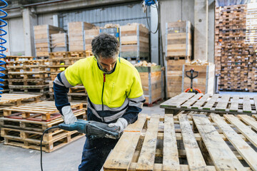 Carpenter cutting wooden pallet with reciprocating saw in a recycling factory, sustainable wood and...