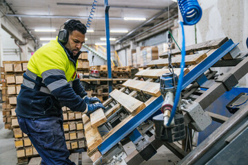Carpenter wearing safety equipment assembling wooden pallets on an automated machine in a recycling...