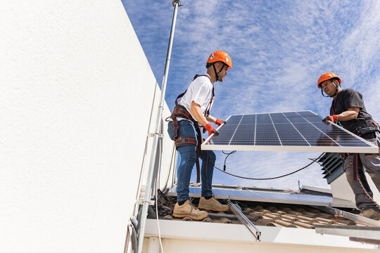 Young technician with colleague installing solar panels on roof