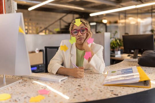Overworked businesswoman with arrow sticky notes all over her sitting at office