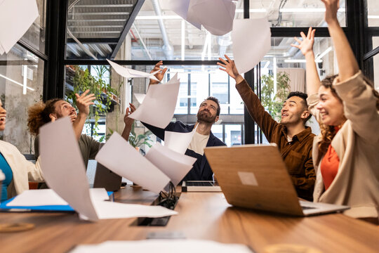 Carefree business colleagues throwing papers in meeting at office