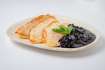 A beautifully arranged plate showcases three golden crepes alongside a vibrant berry sauce and mint