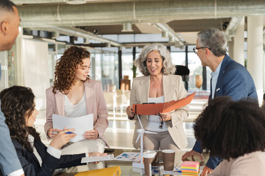 Senior businesswoman holding file conducting meeting with colleagues at office