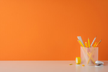 A minimalist desk setup featuring pencils, stationery, and a vibrant orange background, offering...