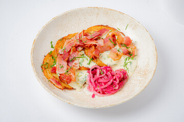A hearty breakfast features crispy bacon on mashed potatoes, topped with pickled onions and herbs