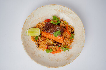 Golden-brown salmon rests on a bed of flavored rice, garnished with fresh herbs and lime