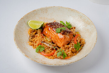 A salmon fillet sits on flavorful rice, garnished with lime and herbs