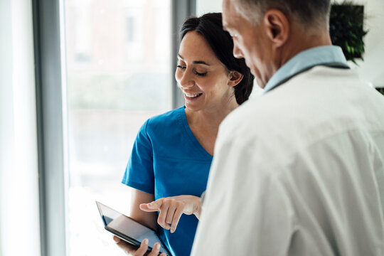 Smiling nurse discussing with doctor over tablet PC in hospital