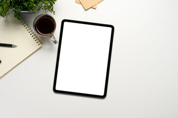 Flat lay of digital tablet mockup on white desk with coffee, notepad, and plant