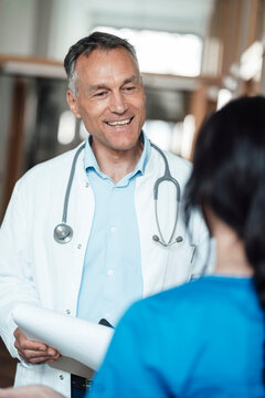 Happy doctor discussing over medical record with nurse in hospital