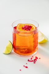A vibrant cocktail sits in a clear glass, garnished with orange and lime, perfect for summer