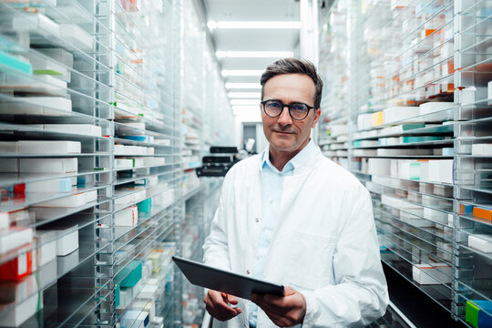 Pharmacist with tablet PC standing in storage room at pharmacy