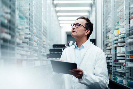 Pharmacist with tablet PC checking medicines on shelf and taking inventory in pharmacy