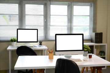 Modern office interior with blank computer monitors, potted plants, and office supplies
