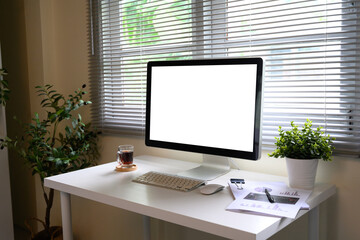Bright office desk scene with desktop computer screen, green plant, coffee, and charts