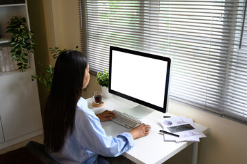 Woman working at a desk with a large computer monitor in a bright home office
