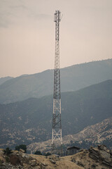 A towering cellular communication tower stands tall against a backdrop of hazy mountains and a vast sky.