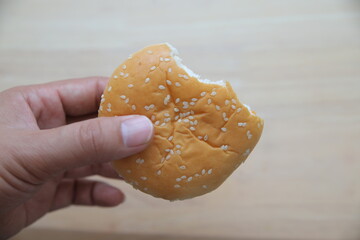 Close-up image of a hand holding a bitten chicken burger filled with crispy fried chicken, cheese,...