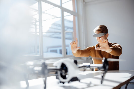 Businessman wearing virtual reality simulator making finger frame sitting with drone at desk