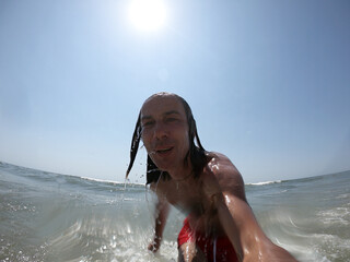 Handsome guy with long hair having fun at beach, sea waves splashing on his body