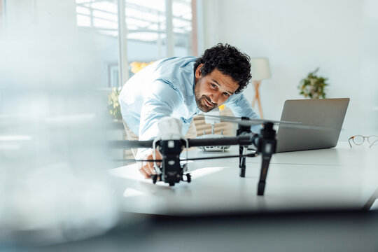 Smiling businessman analyzing drone at desk in office