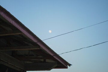 Early evening sky with a visible moon and the roofline of a building. Ideal for twilight scenes or architectural context.