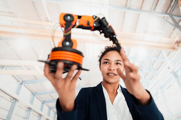Smiling young businesswoman examining robotic arm in factory