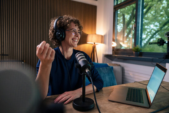 Happy radio DJ wearing headset recording through microphone in studio