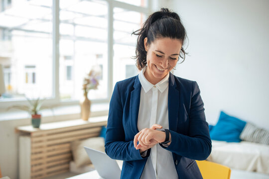 Happy businesswoman checking time on smart watch