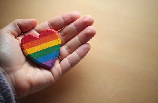 Hand holds vibrant rainbow heart symbol. Represents LGBT pride, equality, and tolerance. Celebrates International Day Against Homophobia, bisexual, gay, lesbian, transgender rights. - Powered by Adobe