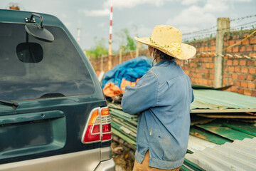 Worker in a straw hat stands by a vehicle near a construction site under a cloudy sky on a late...