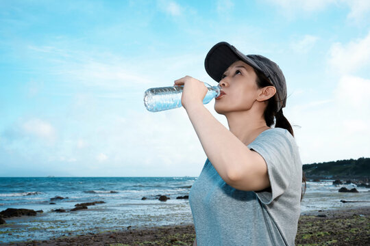 Woman drinking water on the beach enjoying outdoor activity - Powered by Adobe