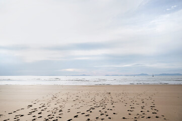 A wide view of a calm beach with footprints on the sand.