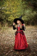 Little girl in witch costume with broom in the forest.