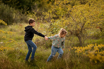 Fototapeta premium Sister pulling brother forward, laughing in autumn woodland.