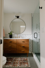 Modern bathroom with wood vanity, round mirror, and glass shower