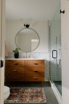 Modern bathroom with wood vanity, round mirror, and glass shower