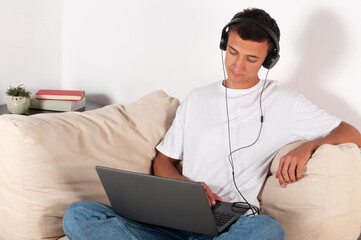 young man with laptop and headphones sitting on sofa at home