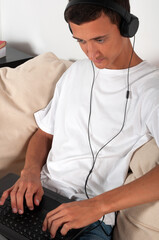 young man with laptop and headphones sitting on sofa at home
