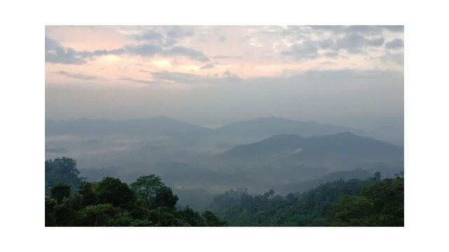 A tranquil sunrise over misty hills, where golden light gently breaks through the clouds, painting the sky above the lush forested valley.