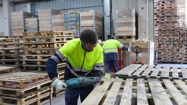 Warehouse worker dismantling wooden pallets with reciprocating saw in slow motion, inside a recycling facility