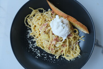 Delicious plate of creamy carbonara pasta topped with a poached egg, served with garlic toast on a...