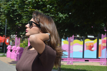 Young caucasian brunette woman in brown dress and sunglasses on city street.
